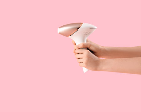 Female hands with modern photoepilator on pink backgroundの写真素材