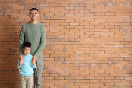 Young man with his little son on brick backgroundの写真素材