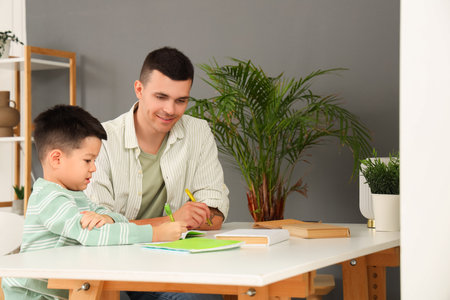 Young man with his little son doing homework at homeの写真素材
