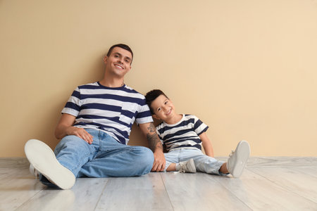 Young man with his little son sitting near beige wallの写真素材