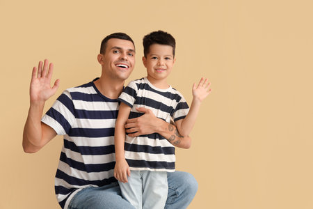 Young man with his little son waving hands on beige backgroundの写真素材