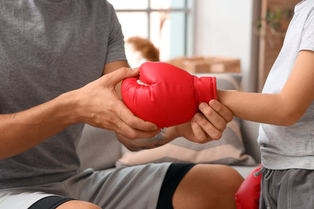 Young man and his little son with boxing glove at home, closeupの写真素材