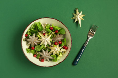 Bowl of salad with beautiful Christmas decorations and fork on green backgroundの写真素材