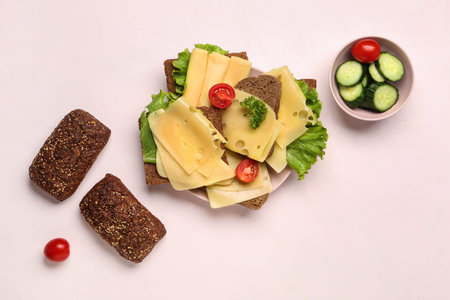 Tasty sandwiches with cheese, tomatoes and cucumber in plate on light backgroundの写真素材
