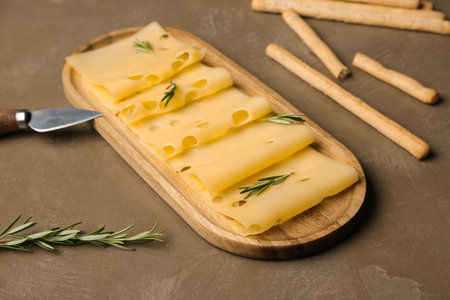 Board with tasty cheese slices, rosemary and Italian Grissini on brown background, closeupの写真素材