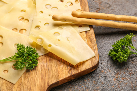Board with tasty cheese slices, parsley and Italian Grissini on grunge background, closeupの写真素材