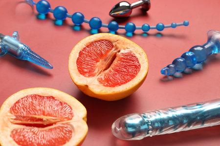 Different sex toys and tasty grapefruit on red background, closeupの写真素材