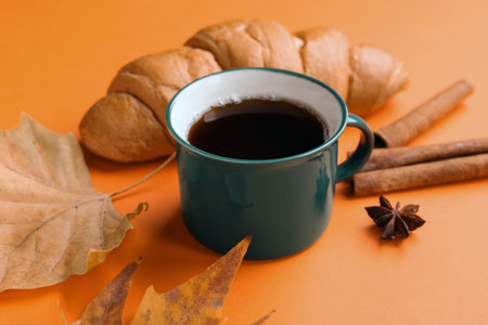 Cup of hot coffee with croissant and autumn leaves on orange background, closeupの写真素材