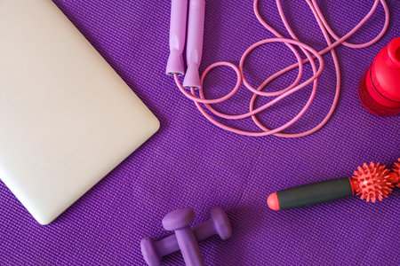 Laptop with sports equipment on violet fitness mat, top view