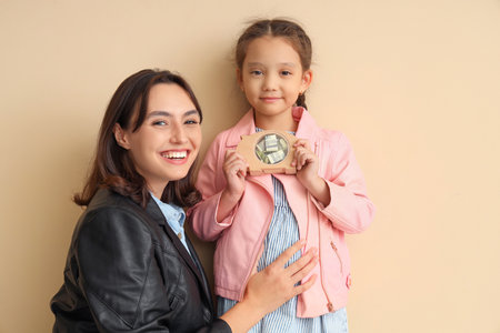 Little girl with piggy bank and her mother on beige backgroundの写真素材