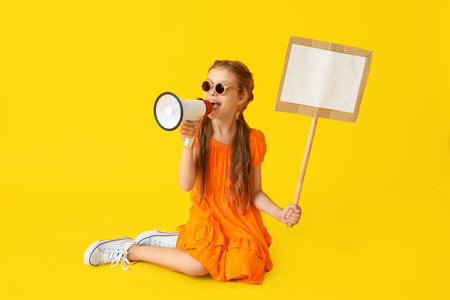 Little girl with megaphone and placard sitting on yellow backgroundの写真素材