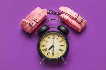 Alarm clock with handcuffs on purple background. Time for sexの写真素材