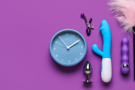 Alarm clock with different toys on purple background. Time for sexの写真素材