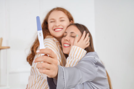 Happy young lesbian couple with pregnancy test hugging in bathroom, closeupの写真素材