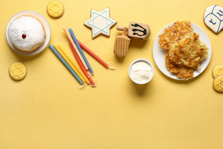 Hannukah composition with potato pancakes, candles, sour cream and dreidels on yellow tableの写真素材