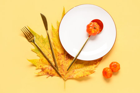 Stylish autumn table setting with maple leaf and pumpkins on yellow backgroundの写真素材