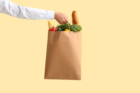 Woman holding paper bag with fresh food on yellow backgroundの写真素材