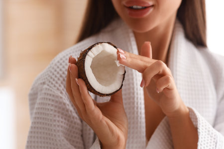 Beautiful young woman with coconut and oil in bathroom, closeupの写真素材