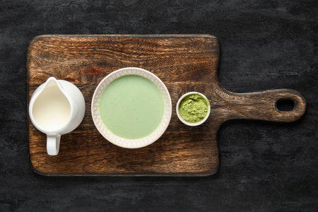 Wooden board with fresh matcha tea, powder and milk on dark backgroundの写真素材