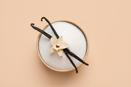 Bowl with aromatic vanilla sugar, flower and sticks on beige background