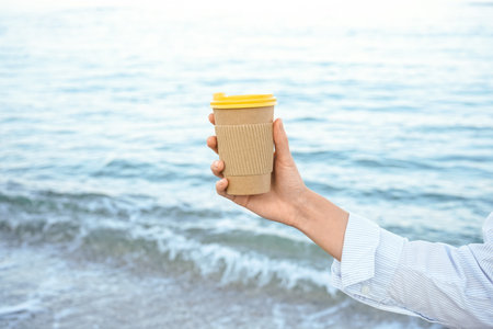 Woman holding paper coffee cup by the seaの写真素材