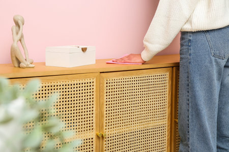 Woman wiping dust on chest of drawers in room