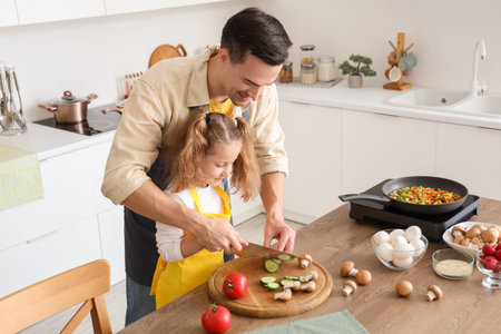 Cute little girl with her dad cutting cucumber in kitchen