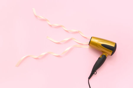 Hair dryer and ribbons on pink backgroundの写真素材