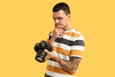 Thoughtful male photographer with modern camera on yellow backgroundの写真素材