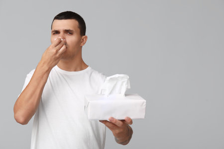 Ill young man with tissues blowing nose on gray backgroundの写真素材