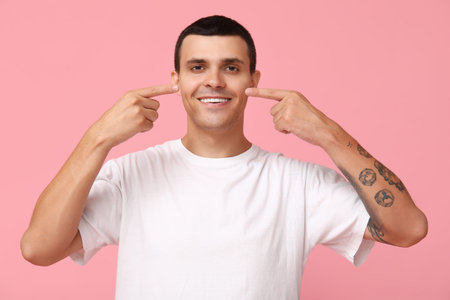 Ill young man pointing at nose on pink background
