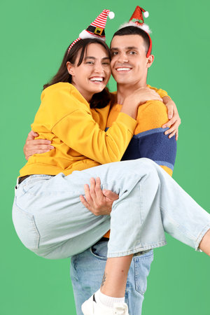 Happy young couple in Christmas hats having fun on green backgroundの写真素材