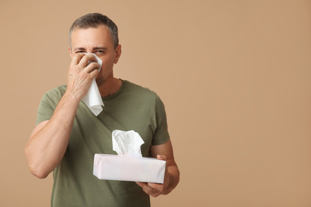 Ill mature man with tissues blowing nose on brown backgroundの写真素材