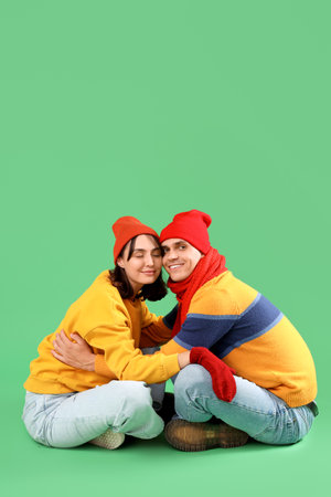 Happy young couple in warm clothes sitting on green backgroundの写真素材