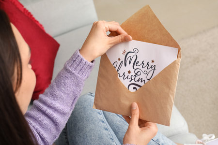 Woman taking Christmas greeting card out from envelope at home, closeupの写真素材