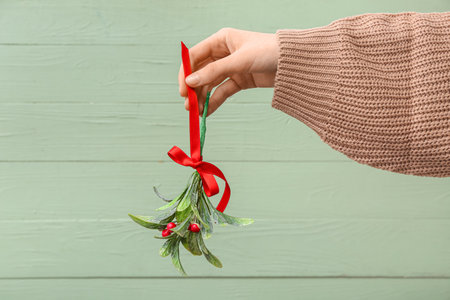 Female hand with mistletoe branch on green wooden backgroundの写真素材