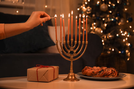 Woman lighting menorah candles on coffee table at evening. Hanukkah celebration