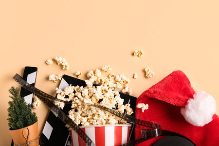 Movie clapper with bucket of popcorn, film reel and Santa hat on beige backgroundの写真素材