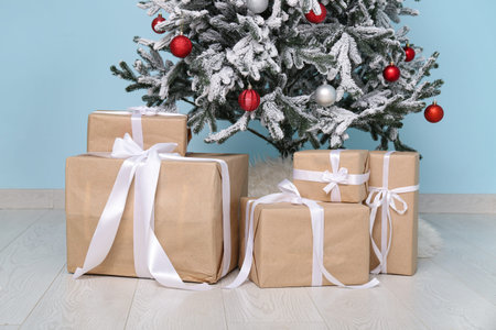 Beautiful decorated Christmas tree with gifts near blue wall