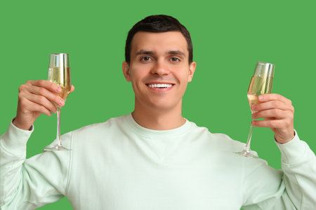 Happy young man with glasses of champagne celebrating Christmas on green backgroundの写真素材