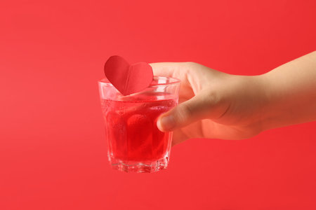 Female hand with glass of cocktail tasty on red background. Valentine's Day celebrationの写真素材