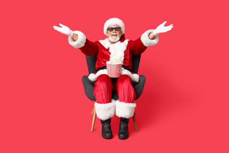Happy Santa Claus in 3D glasses with bucket of tasty popcorn on red backgroundの写真素材