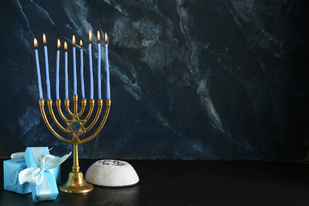 Menorah with burning candles, gifts and kippah for Hanukkah celebration on dark backgroundの写真素材