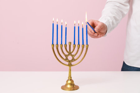 Man lighting candles in menorah on pink background, closeup. Hanukkah celebrationの写真素材