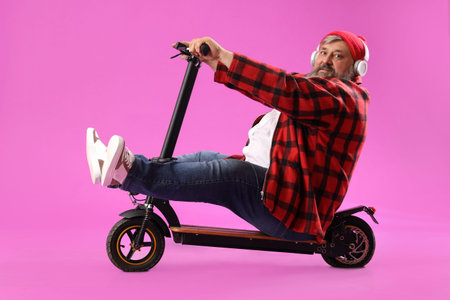 Mature man in headphones with electric scooter on purple background