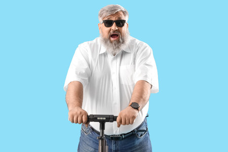 Shocked mature man riding electric scooter on blue backgroundの写真素材