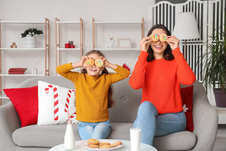 Funny mother and her little daughter eating cookies with milk at homeの写真素材