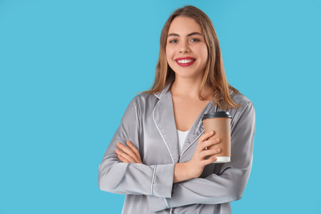 Portrait of pretty young woman in pajamas with takeaway coffee cup on blue backgroundの写真素材