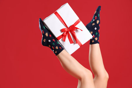 Woman in Christmas socks with gift box on red backgroundの写真素材