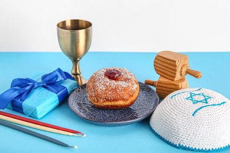 Gift box with dreidels, candles, cup and tasty donut on blue table near white wall. Hanukkah celebrationの写真素材
